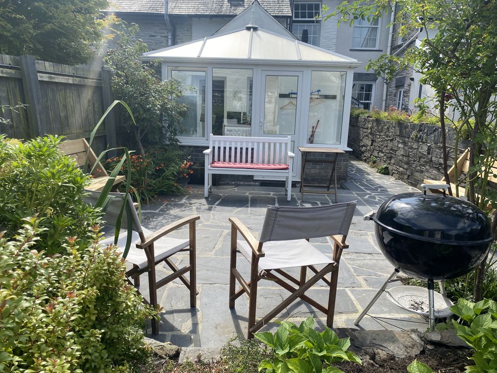 A garden with a conservatory and seating area at Swn Yr Afon Abergynolwyn near Tywyn