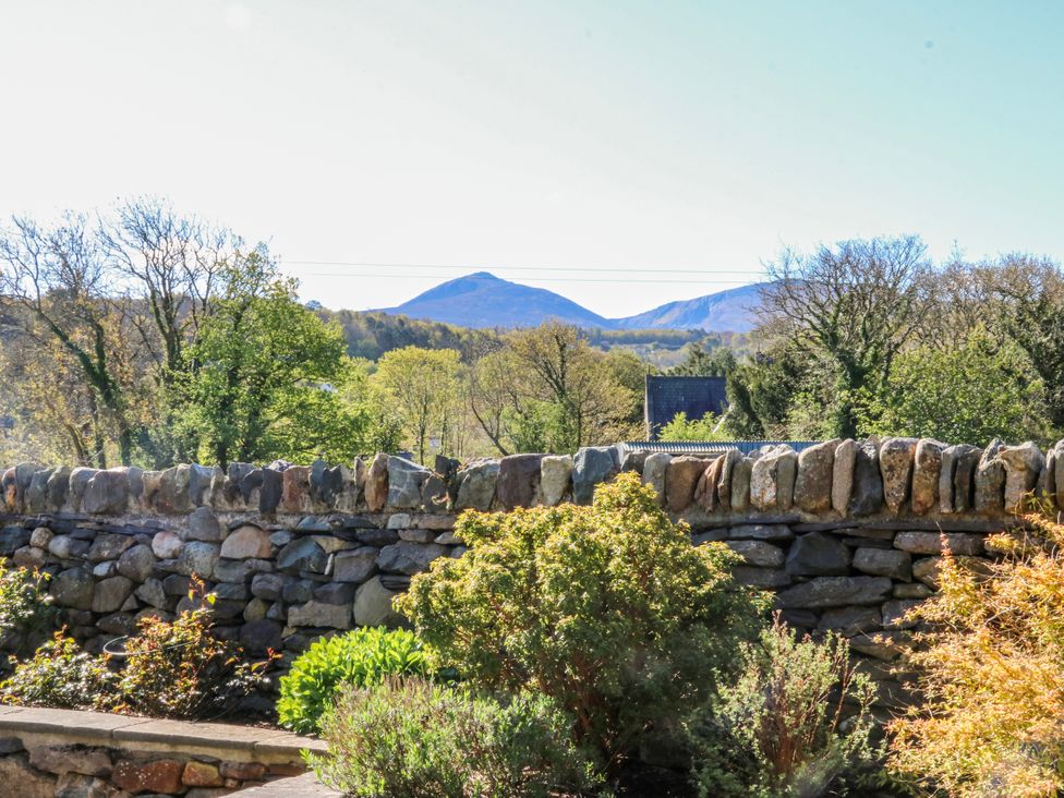 A garden view with a stone wall and mountains in the background at Bronfa in Tregarth
