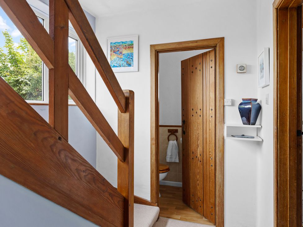 A hallway with a staircase and door leading to a bathroom at 7 Duporth Bay in St. Austell