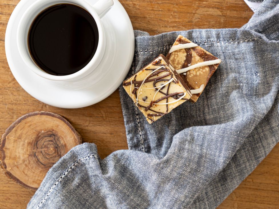 A coffee cup with cookies on a napkin and wooden coaster