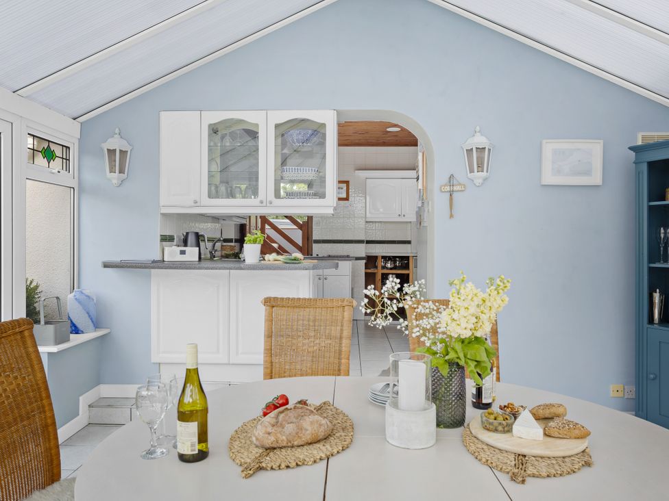 A conservatory with dining table and access to kitchen at 7 Duporth Bay in St. Austell