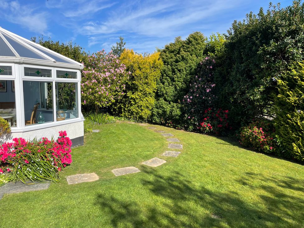 A garden with a conservatory and flower beds at Blue Haze, Duporth Bay, Charlestown