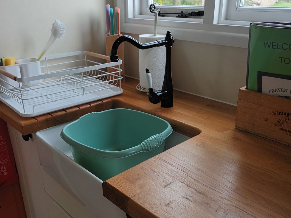 A kitchen with a sink, tap, draining rack, and bucket at The Herdsman Luxury Shepherds Hut in Barnoldswick