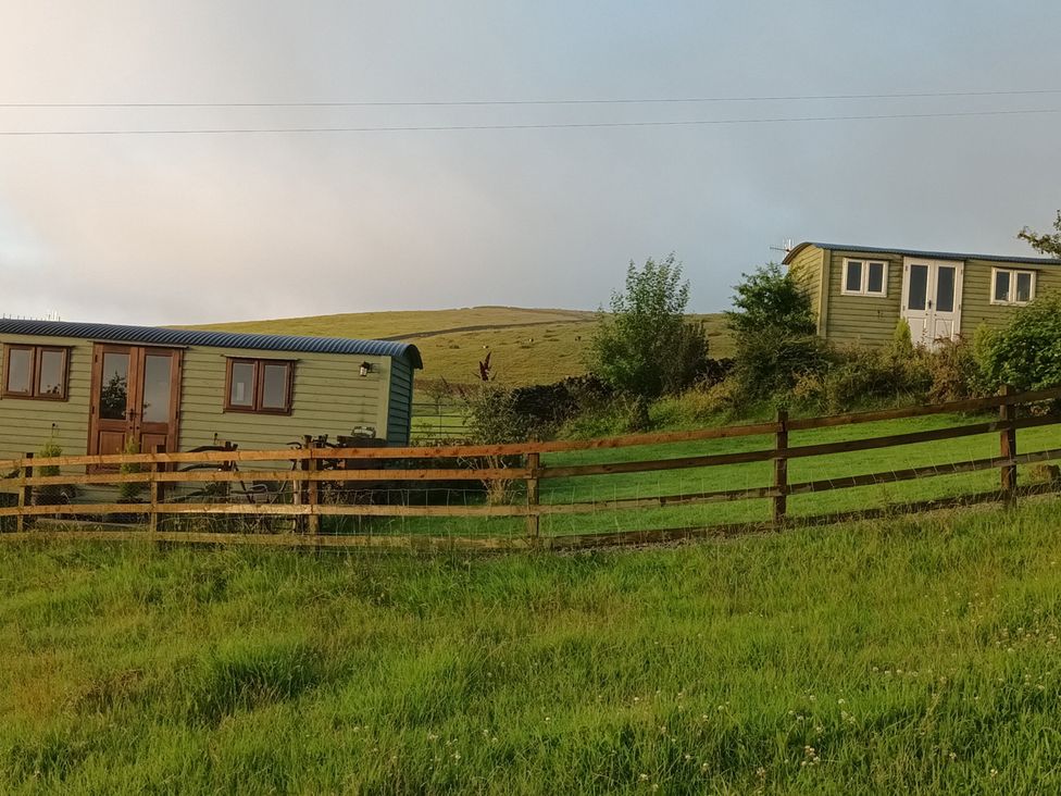 Two green huts with a fence and grass at The Herdsman Luxury Shepherds Hut in Barnoldswick