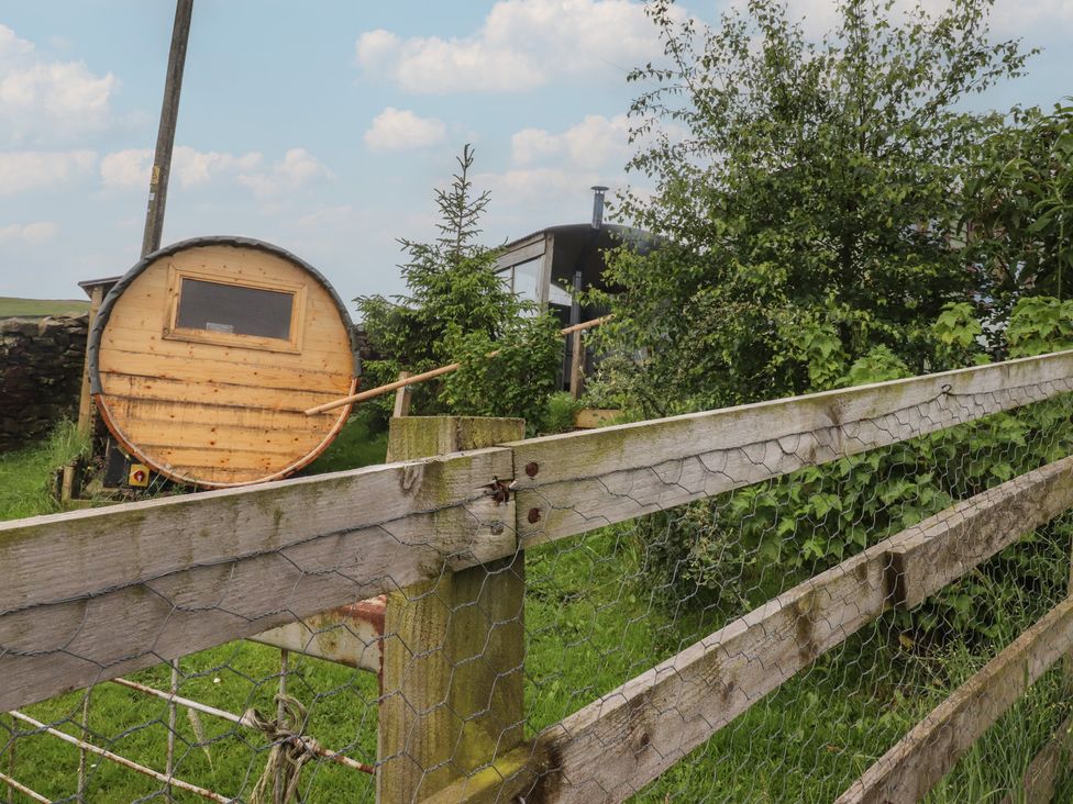 A shepherd's hut beside a fence and tree at The Herdsman Luxury Shepherds Hut in Barnoldswick