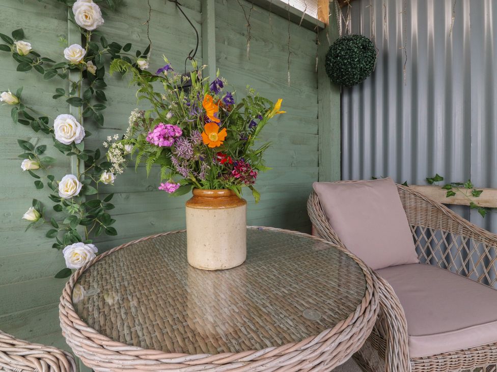 A flower vase on a wicker table in an outdoor seating area at The Herdsman Luxury Shepherds Hut Barnoldswick