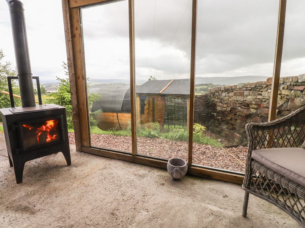 A conservatory with a wood stove and chair at The Herdsman Luxury Shepherds Hut Barnoldswick