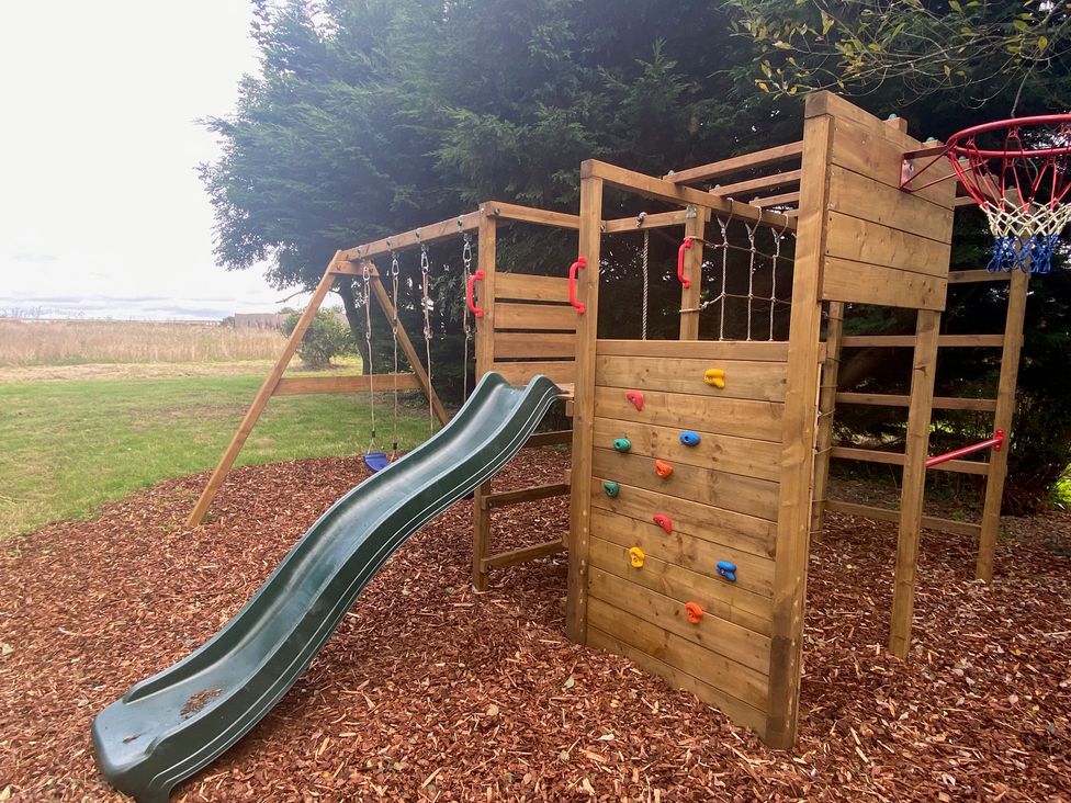 A playset with a slide and climbing wall in an outdoor play area at The Hollies Thurstonfield near Carlisle
