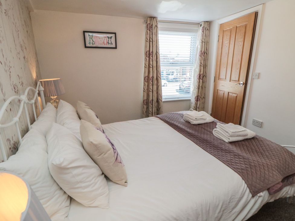 A bedroom with a bed, lamp, and window at Bluebell Cottage in Flamborough