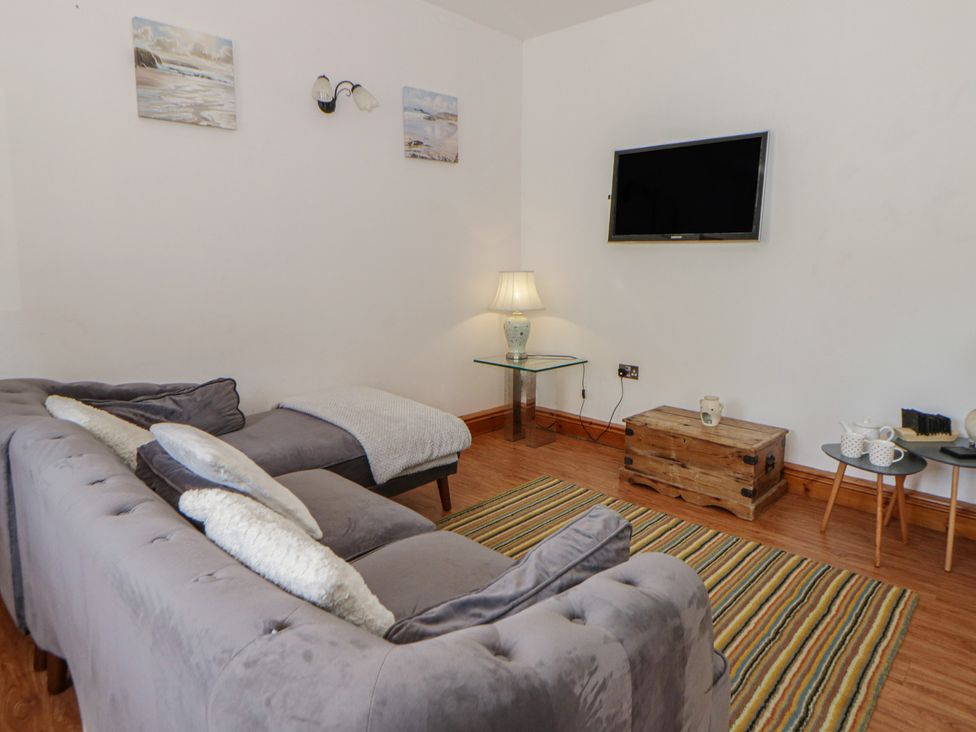 A living room with a sofa, lamp, and television at Swallows Retreat in Tenby