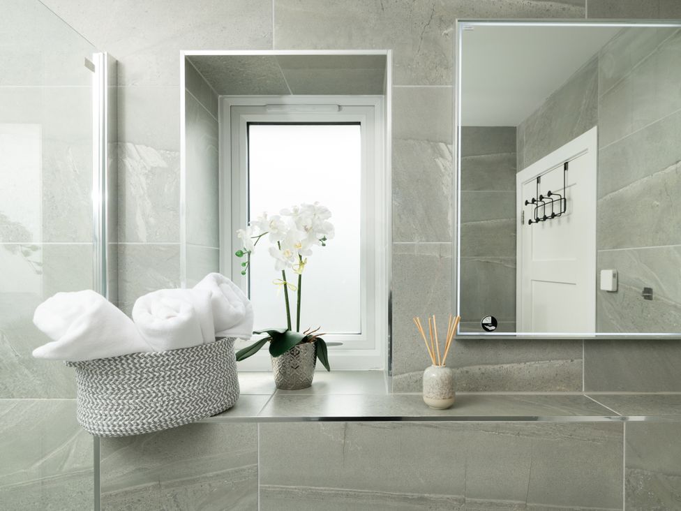 A bathroom with towels and an orchid on a shelf at Sandy Cove in Praa Sands