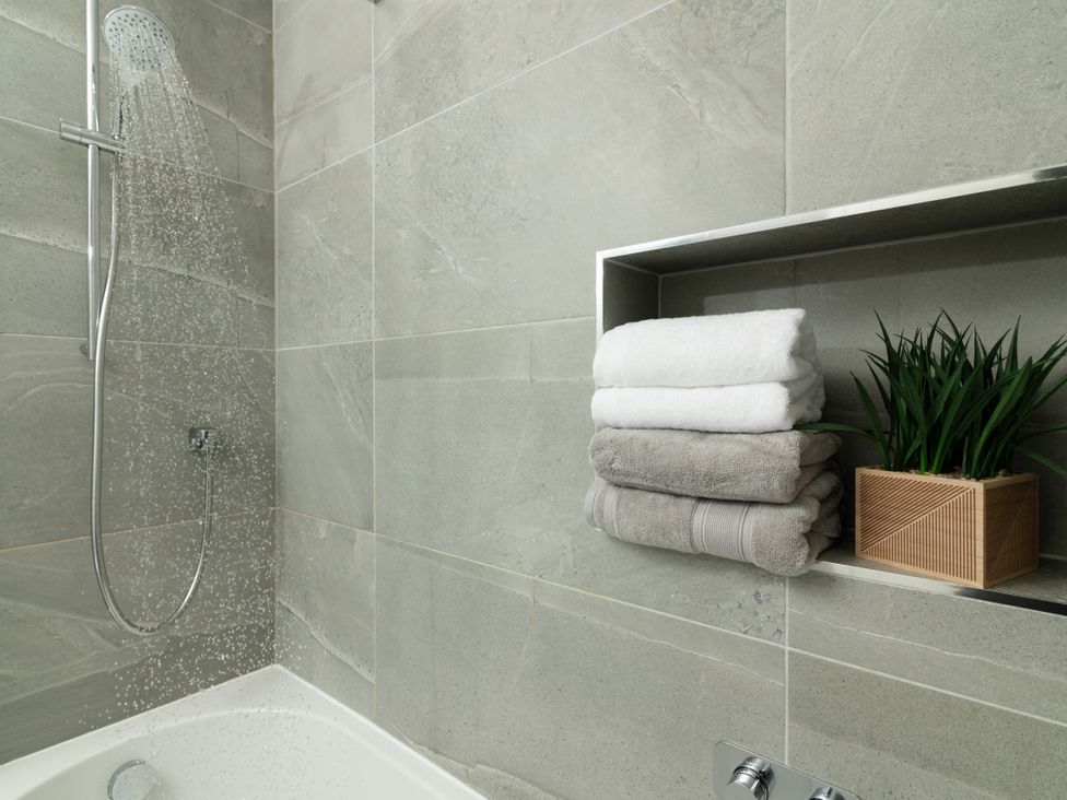 A bathroom with a shower head and towels stacked on a shelf at Sandy Cove in Praa Sands