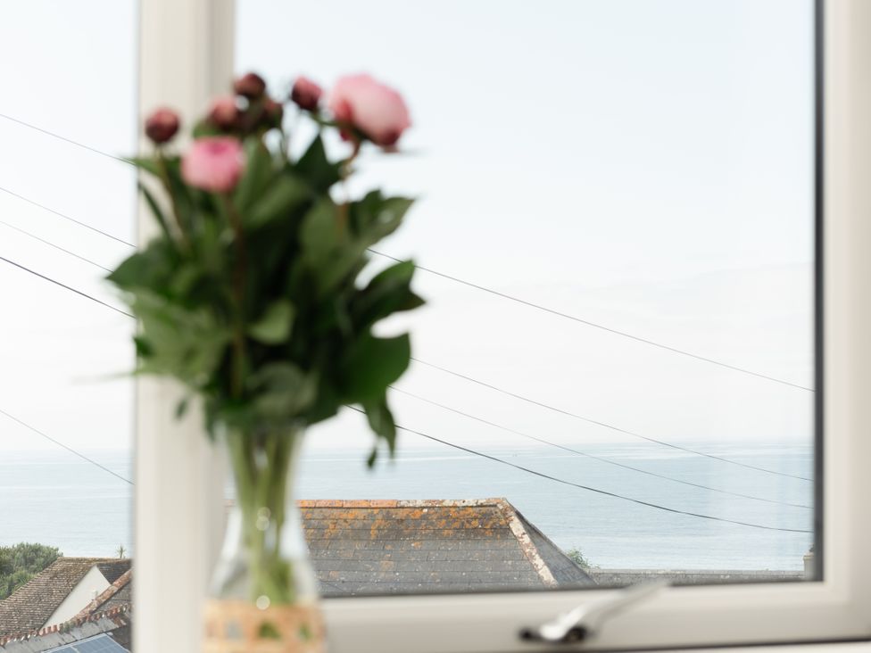 A view of flowers in a vase and the ocean from a window at Sandy Cove in Praa Sands
