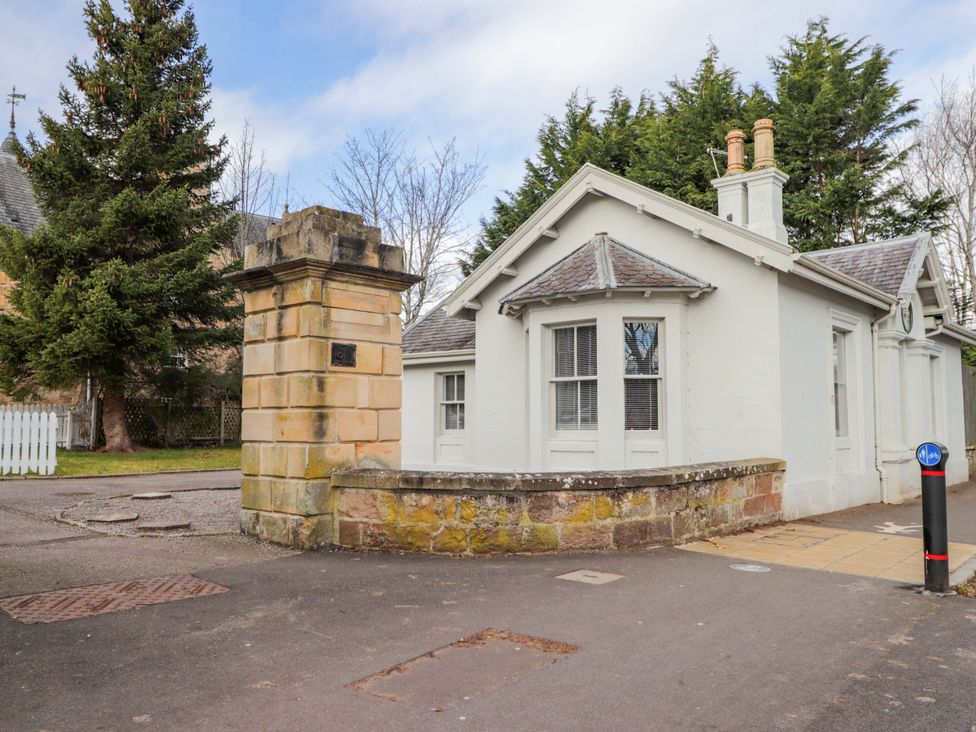 A house with a stone wall and trees at Porter's Lodge Inverness