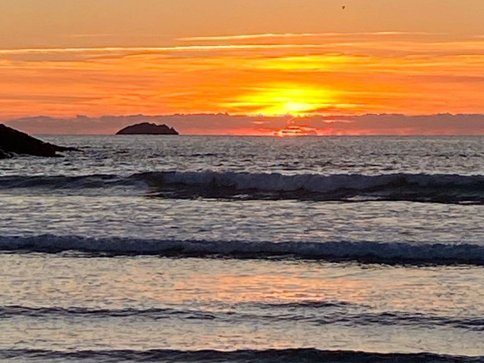A sunset over the sea with waves and an island in the distance at Kirland in St Kew Highway