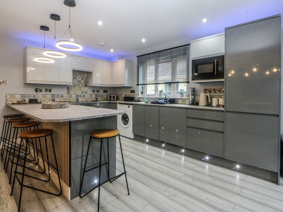 A kitchen with bar stools and a washing machine at Ty Glan Morfa in Morfa Bychan