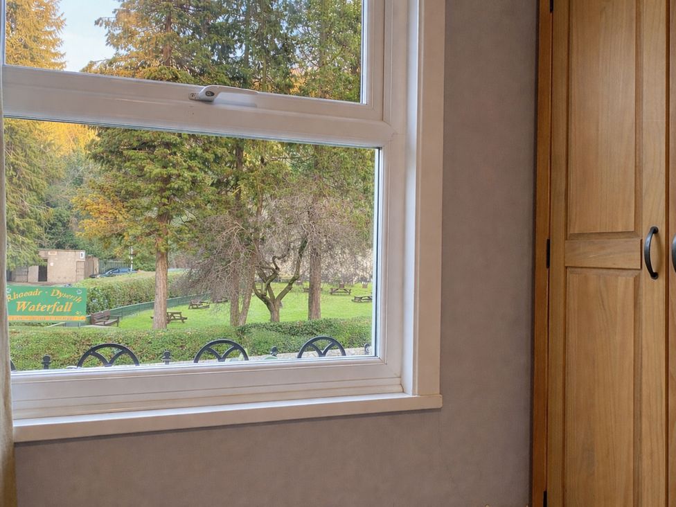 A window view showing trees and a garden at Waterfall Cottage in Dyserth