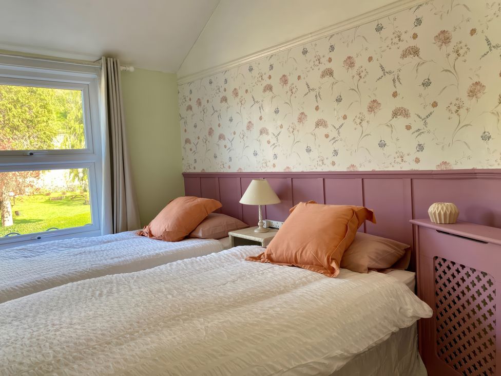 A bedroom with two beds and a window overlooking a garden at Waterfall Cottage in Dyserth