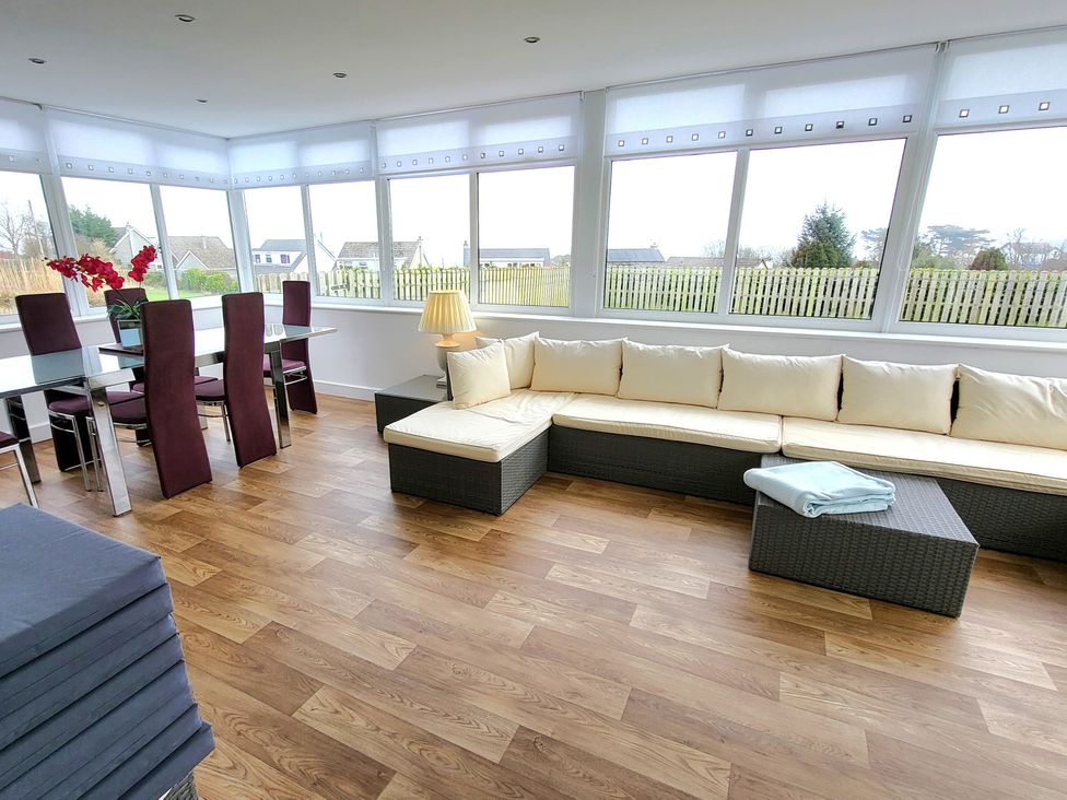 A conservatory with a dining table and chairs and a sofa at Top Of The Lane Luxury Holiday Apartment, Benllech