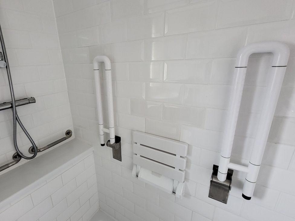 A bathroom with grab bars and a folding bench at Top Of The Lane Luxury Holiday Apartment in Benllech