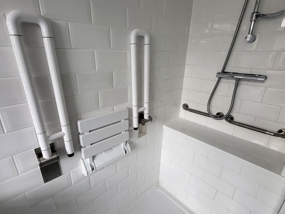 A bathroom with grab bars and a folding shower seat at Top Of The Lane Luxury Holiday Apartment in Benllech