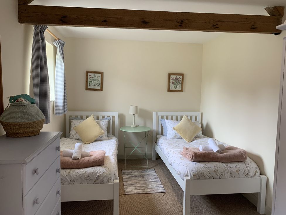 A bedroom with two beds, a side table, and a lamp at The Old Dairy in Colyton