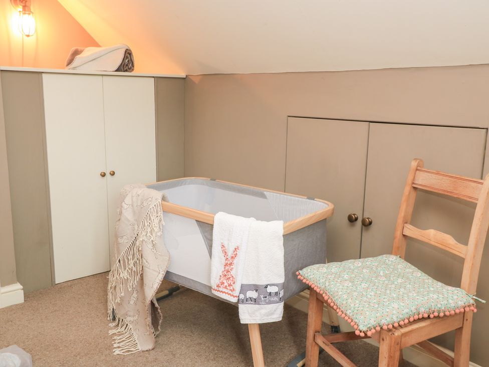 A nursery with a crib and a chair at Pudding Hill Barn Cottage Bibury