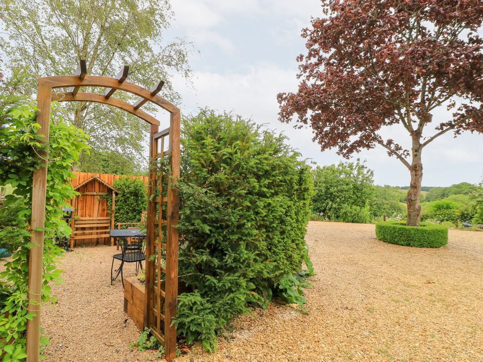 An outdoor area with an archway leading to seating and greenery at Pudding Hill Barn Cottage Bibury