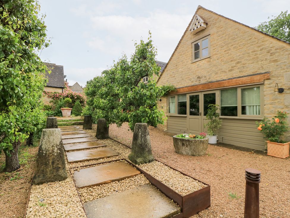 A garden with a stone path and trees at Pudding Hill Barn Cottage Bibury
