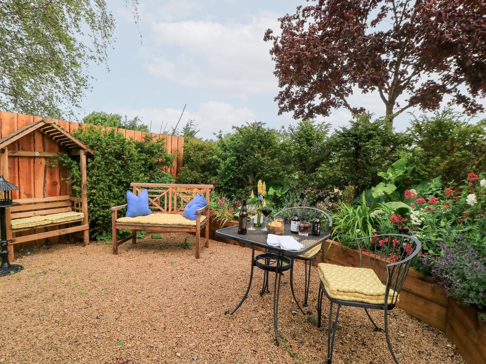 A garden with a bench and table surrounded by plants at Pudding Hill Barn Cottage, Bibury
