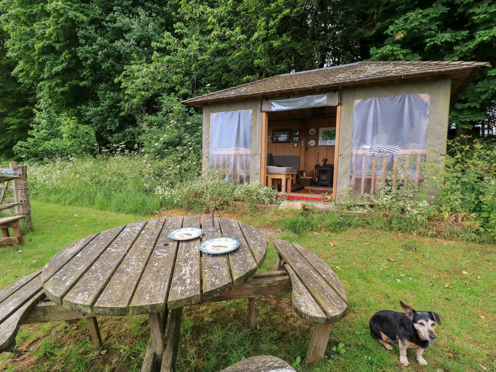 A cabin in a garden with a wooden table and chairs at Pudding Hill Barn Cottage Bibury