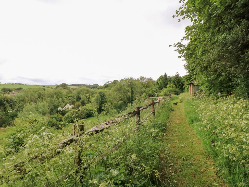A path beside a fence leading through grass and trees at Pudding Hill Barn Cottage Bibury