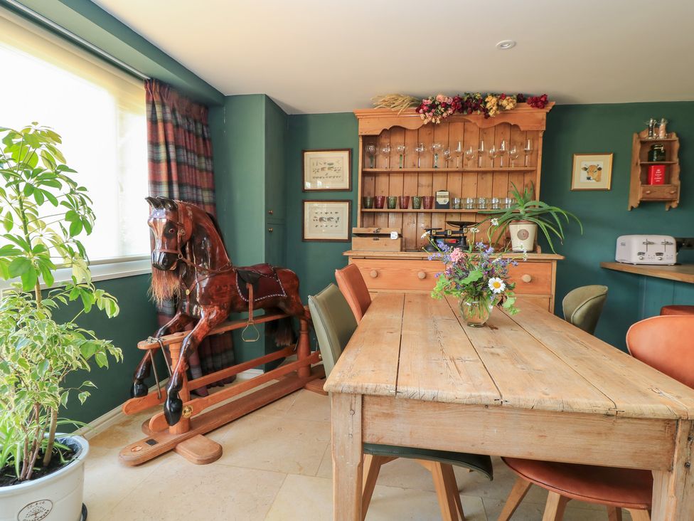 A dining room with a table and rocking horse at Pudding Hill Barn Cottage Bibury