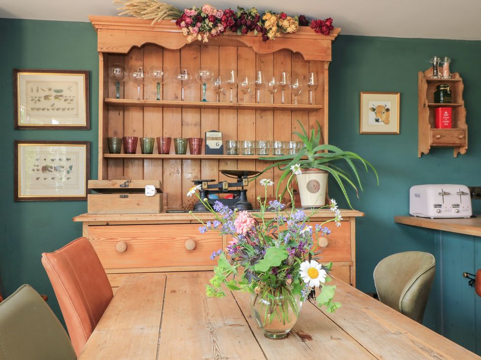 A dining room with a table and shelves displaying glasses at Pudding Hill Barn Cottage in Bibury