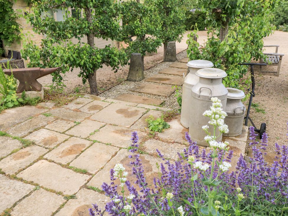 An outdoor area with trees, milk churns, and a pathway at Pudding Hill Barn Cottage Bibury