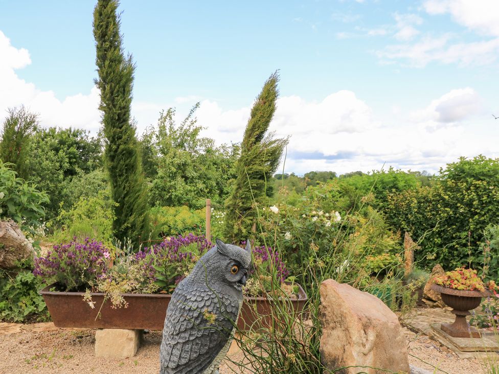A garden with an owl statue and flowers at Pudding Hill Barn Cottage Bibury