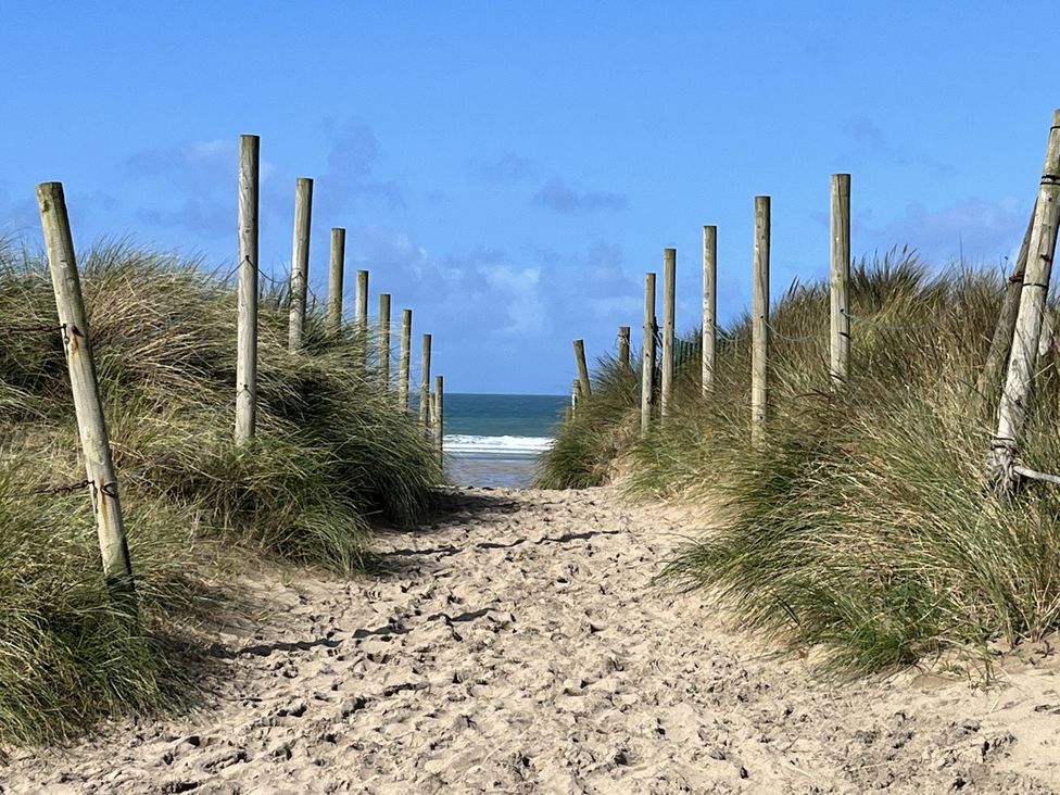 A sandy pathway leading to the beach with grass and wooden posts at Kippy Cottage in Truro