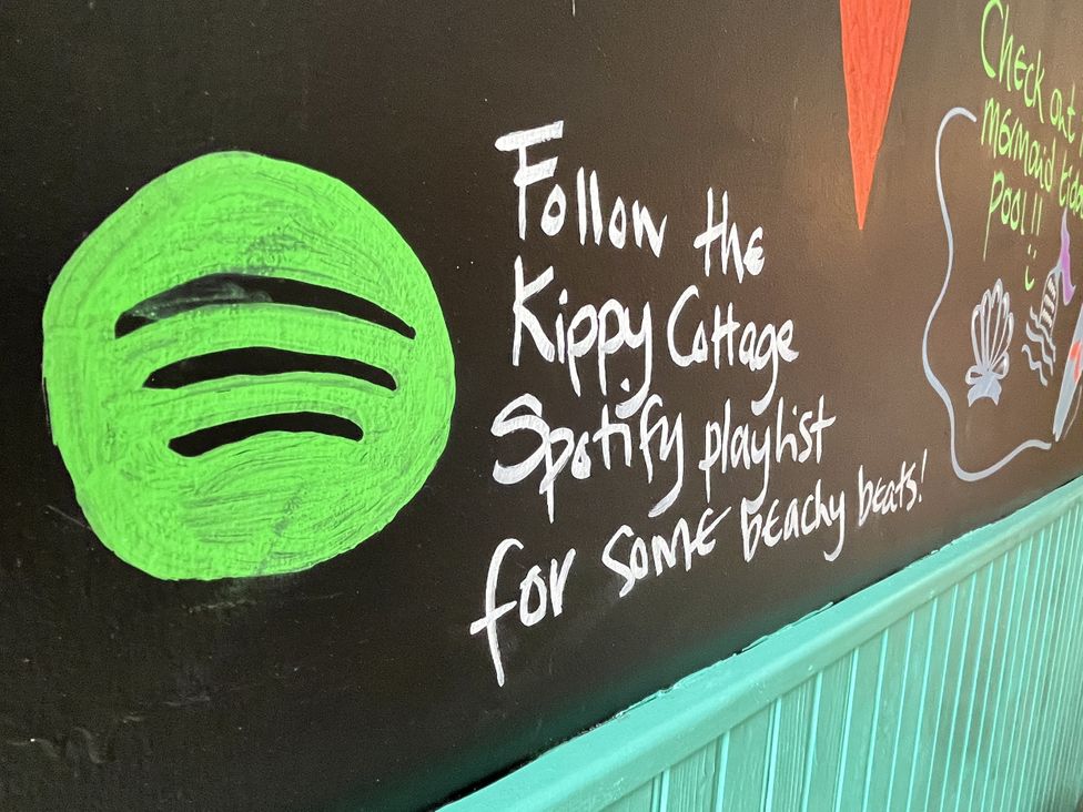 A wall with Spotify logo and text about a playlist at Kippy Cottage in Porthtowan