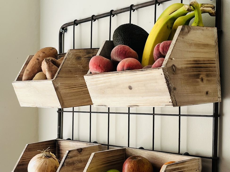 A rack with wooden baskets holding various fruits and vegetables at Kippy Cottage Porthtowan