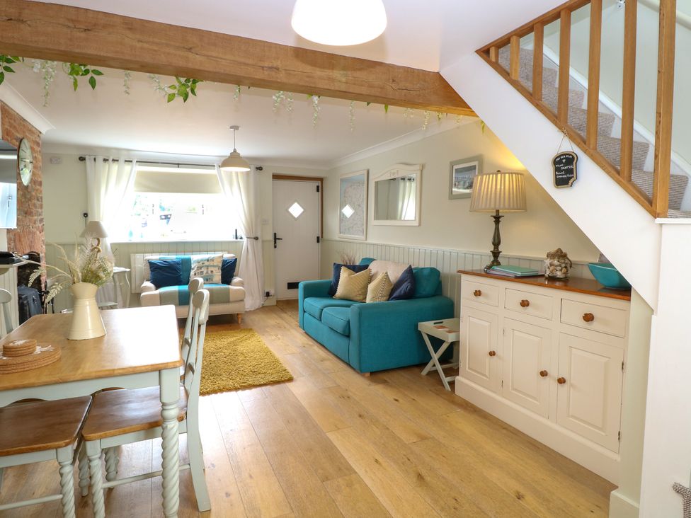 A living room with blue sofas a wooden dining table and chairs and a cabinet under the stairs at Herbies Cottage in Snettisham