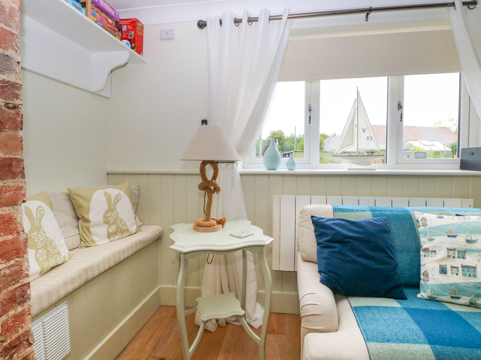 A corner of a living room with a cushioned bench with rabbit pillows a small side table with a lamp and a sofa with blue cushions at Herbies Cottage in Snettisham
