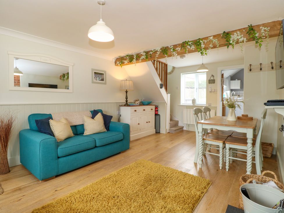 A living room with a blue sofa and cushions a wooden dining table with chairs and a yellow rug at Herbies Cottage in Snettisham