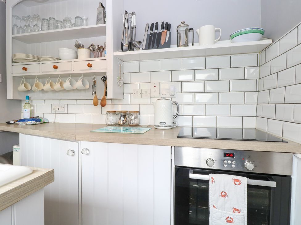 A kitchen countertop with a kettle jars knives and hanging cups at Herbies Cottage in Snettisham