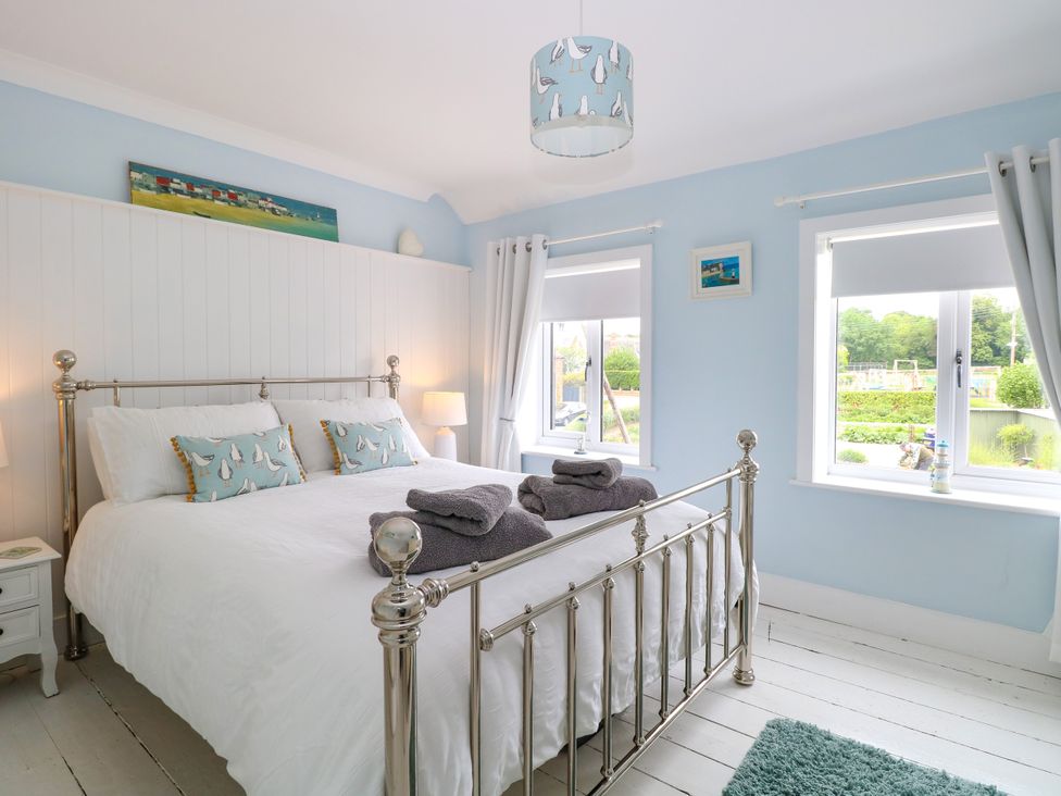 A bedroom with a metal bed frame white bedding blue walls and two windows at Herbies Cottage in Snettisham