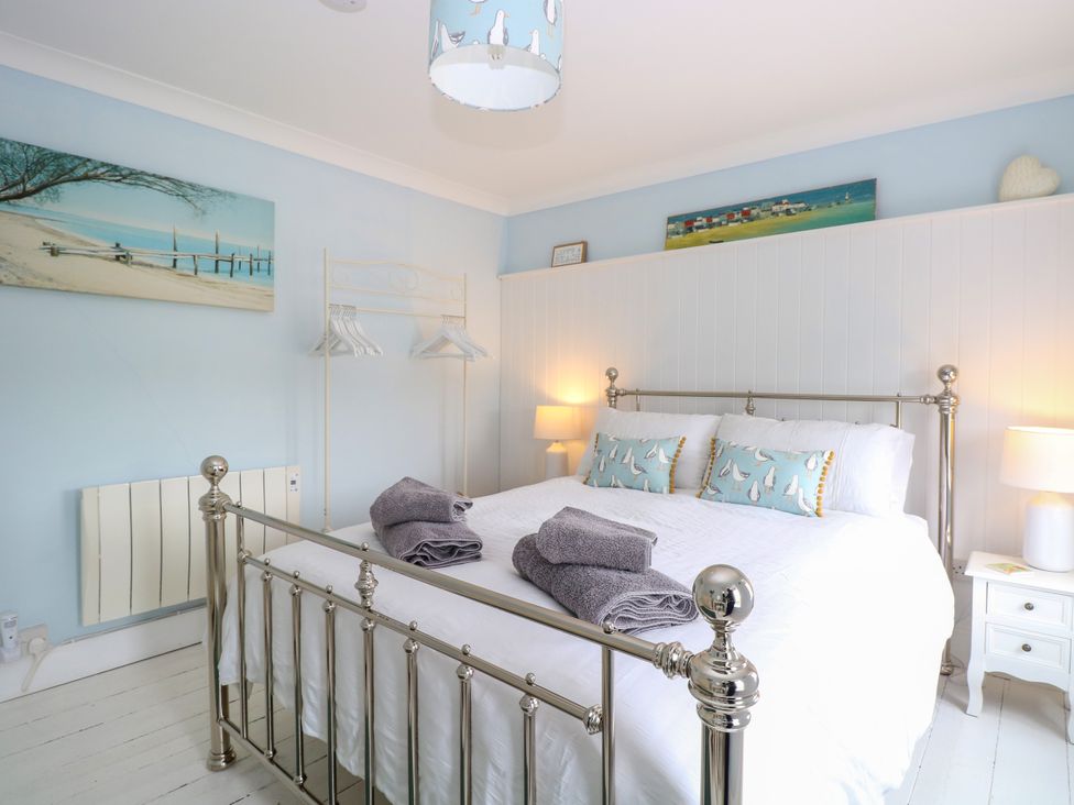 A bedroom with a metal bed frame white bedding with folded towels and sea bird pillows next to two bedside tables with lamps and wall art at Herbies Cottage in Snettisham