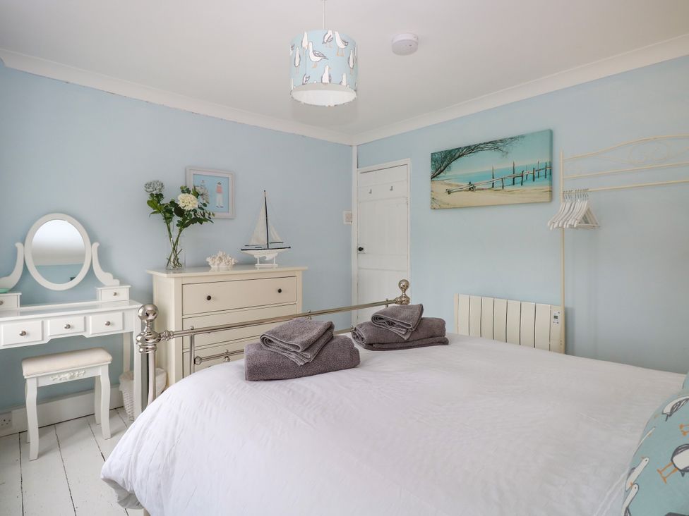 A bedroom with a bed with towels on it a white dresser with flowers and a sailboat and a dressing table at Herbies Cottage in Snettisham