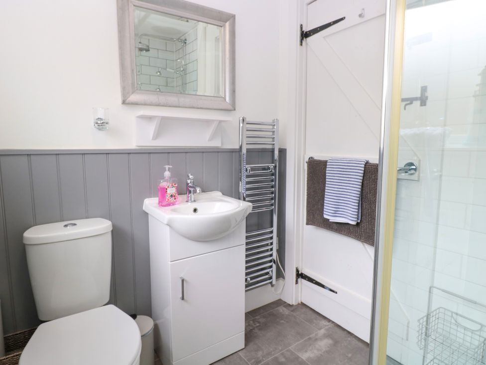 A bathroom with a toilet sink mirror towel rack and shower at Herbies Cottage in Snettisham