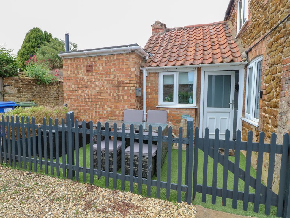 An outdoor patio area with a glass table and four chairs behind a black picket fence at Herbies Cottage in Snettisham