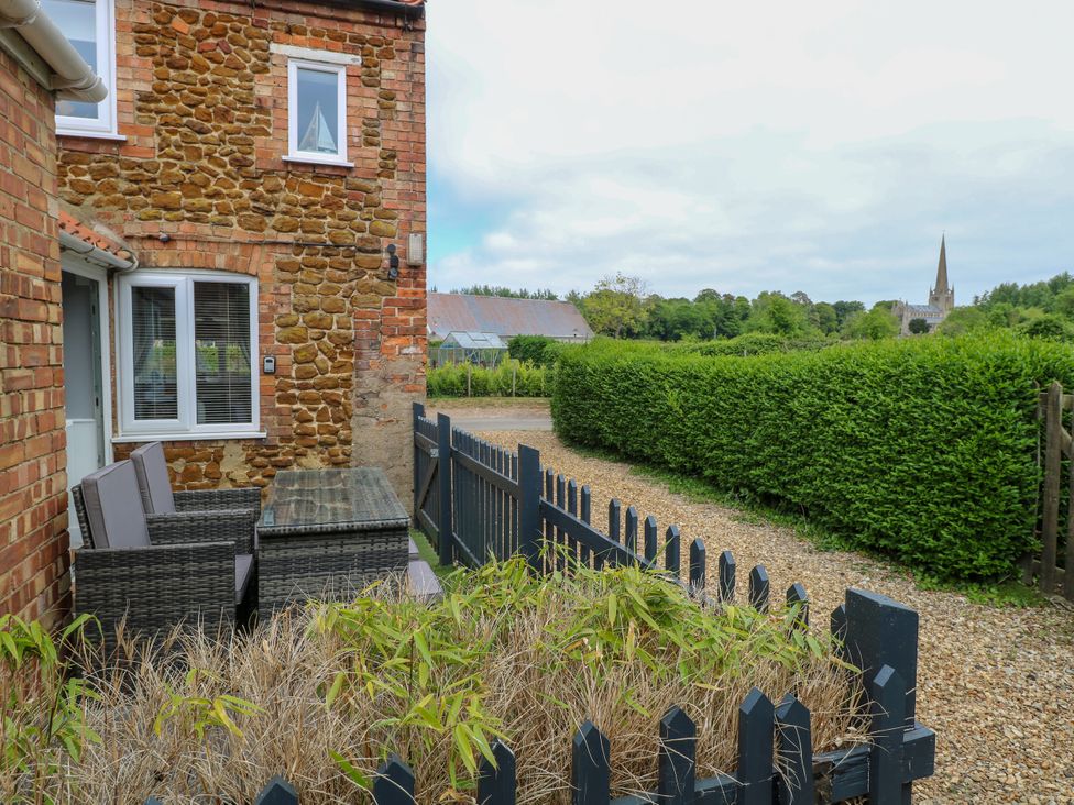A stone and brick house with patio furniture outside a fenced garden and a gravel path at Herbies Cottage Snettisham