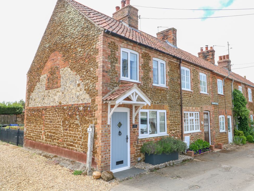 A row of brick and stone cottages with tile roofs and white framed windows on a street at Herbies Cottage in Snettisham